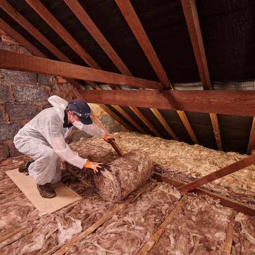 A contractor laying mineral wool insulation down in a loft